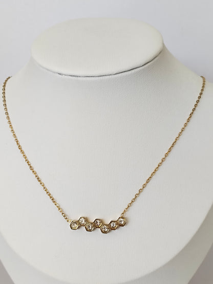 A delicate gold chain necklace with five small, clear, round-cut stones set in a row, displayed on a white jewelry bust.