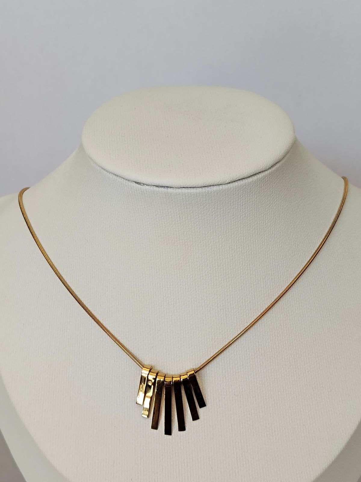 A gold chain necklace with a central cluster of alternating gold and black bar pendants, displayed on a white neck mannequin.