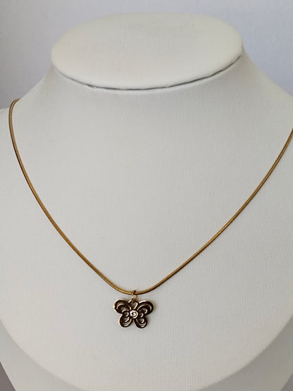 A delicate gold chain necklace with a small, textured flower-shaped pendant, displayed on a white fabric jewelry bust.