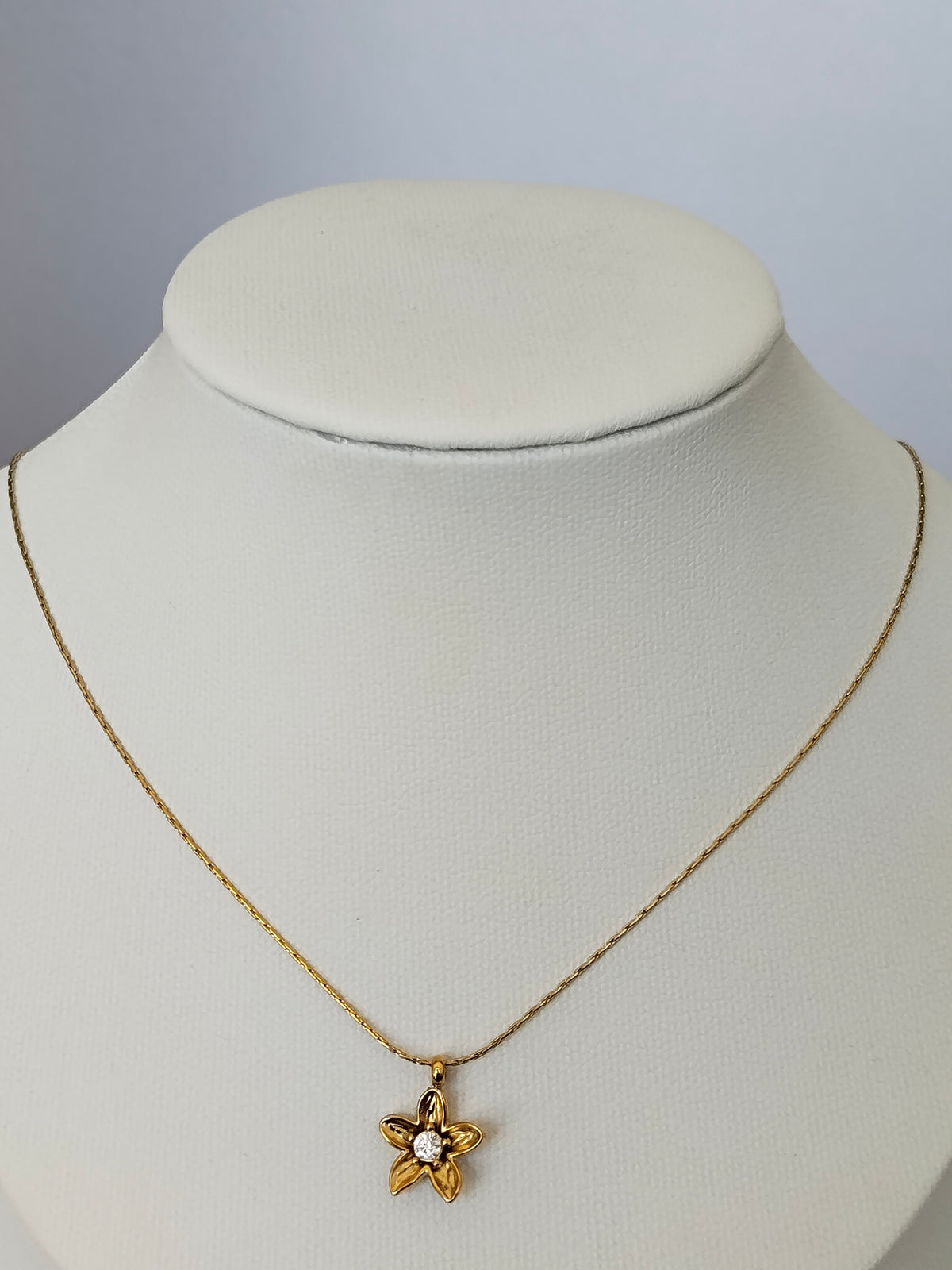 A gold star-shaped pendant necklace with a clear central stone, displayed on a white jewelry bust against a light gray background.