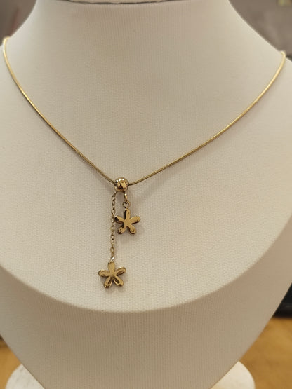 A gold chain necklace displayed on a cream-colored jewelry bust, featuring a central charm with two dangling flower-like charms.