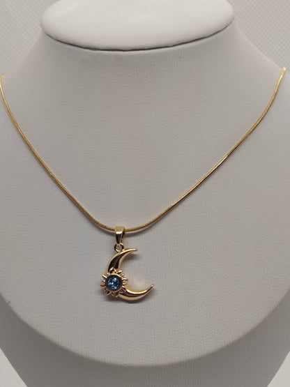 A gold chain necklace with a crescent moon pendant featuring a small blue gemstone, displayed on a white jewelry bust.