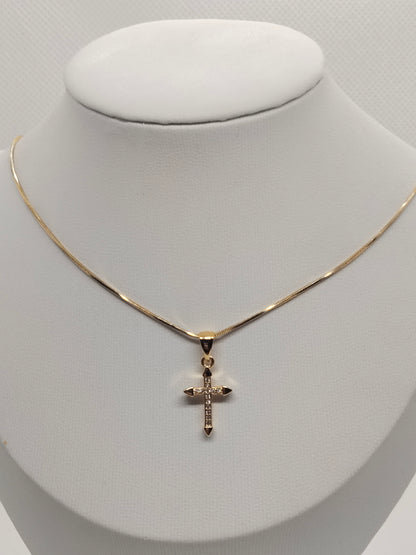 A delicate gold chain necklace with a small cross pendant, displayed on a white jewelry bust.