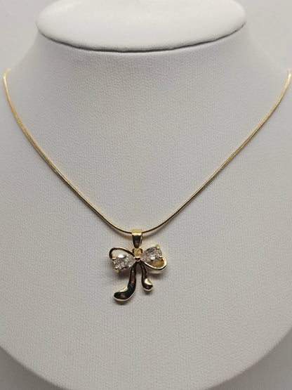 A gold necklace with a bow-shaped pendant set with clear rhinestones, displayed on a white jewelry bust.