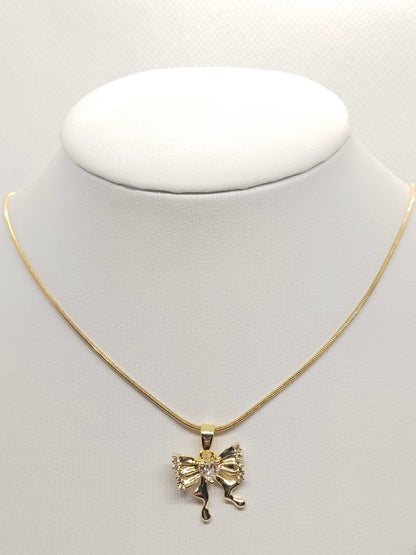 A gold chain necklace with a bow-shaped pendant featuring a central clear rhinestone, displayed on a white jewelry bust against a light gray background.