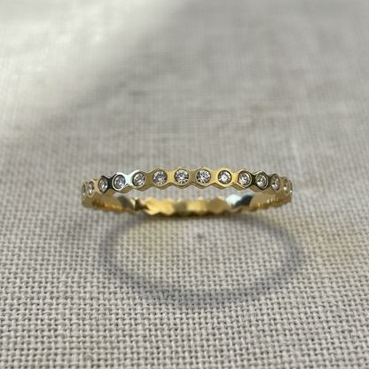 A gold eternity ring featuring a row of small clear round-cut stones set in a honeycomb pattern, resting on a textured beige linen fabric.