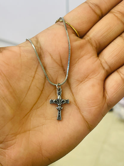 A silver cross pendant necklace with a textured chain, held in the palm of a hand.