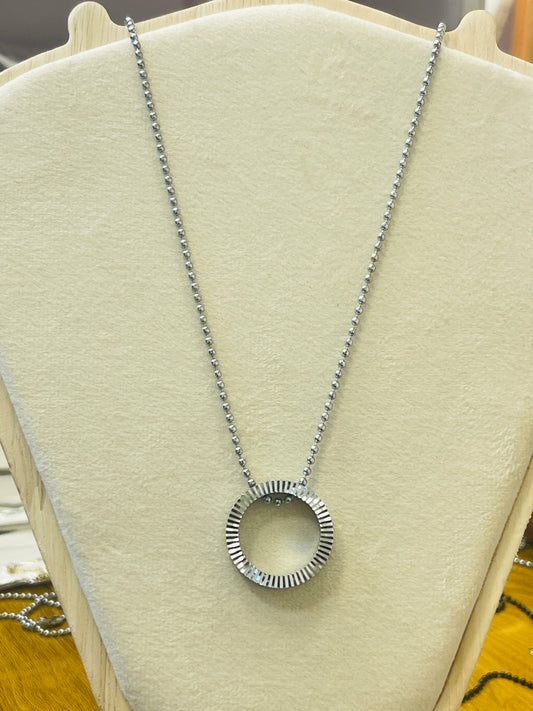 A silver pendant necklace with a textured, ridged circular ring on a silver ball chain, displayed on a cream-colored jewelry bust.