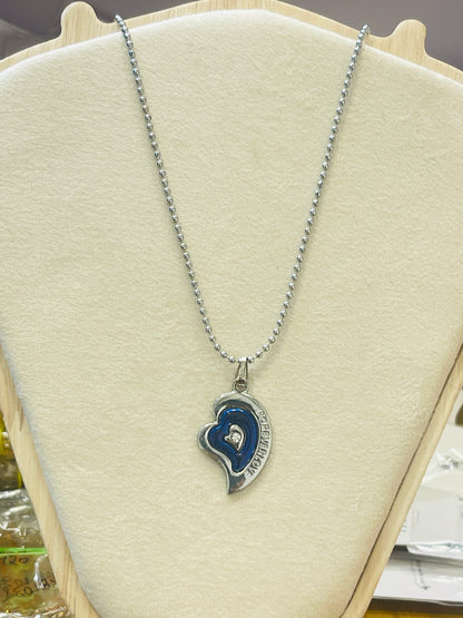 A silver ball-chain necklace with a heart-shaped pendant featuring a blue enamel inlay and a small clear center stone, displayed on a cream-colored jewelry bust.