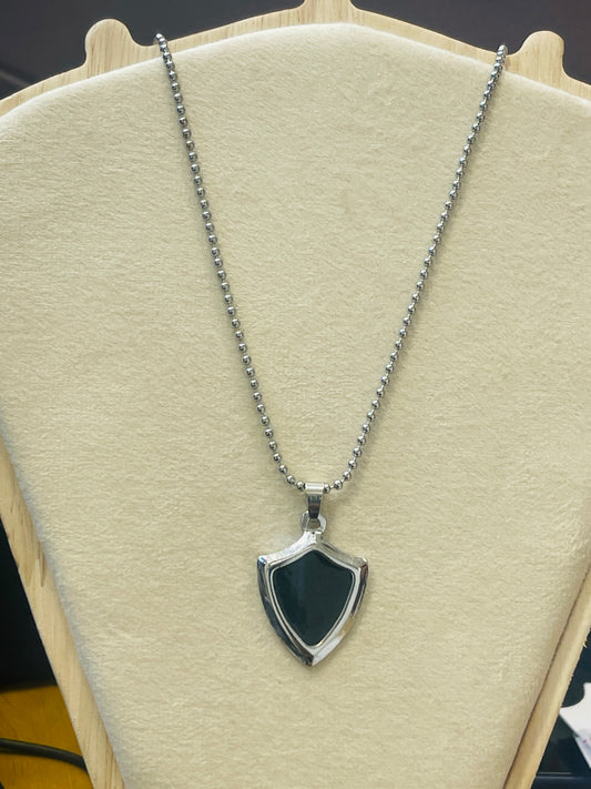 A silver-tone shield-shaped pendant necklace with a dark green inlay, displayed on a cream-colored jewelry bust.