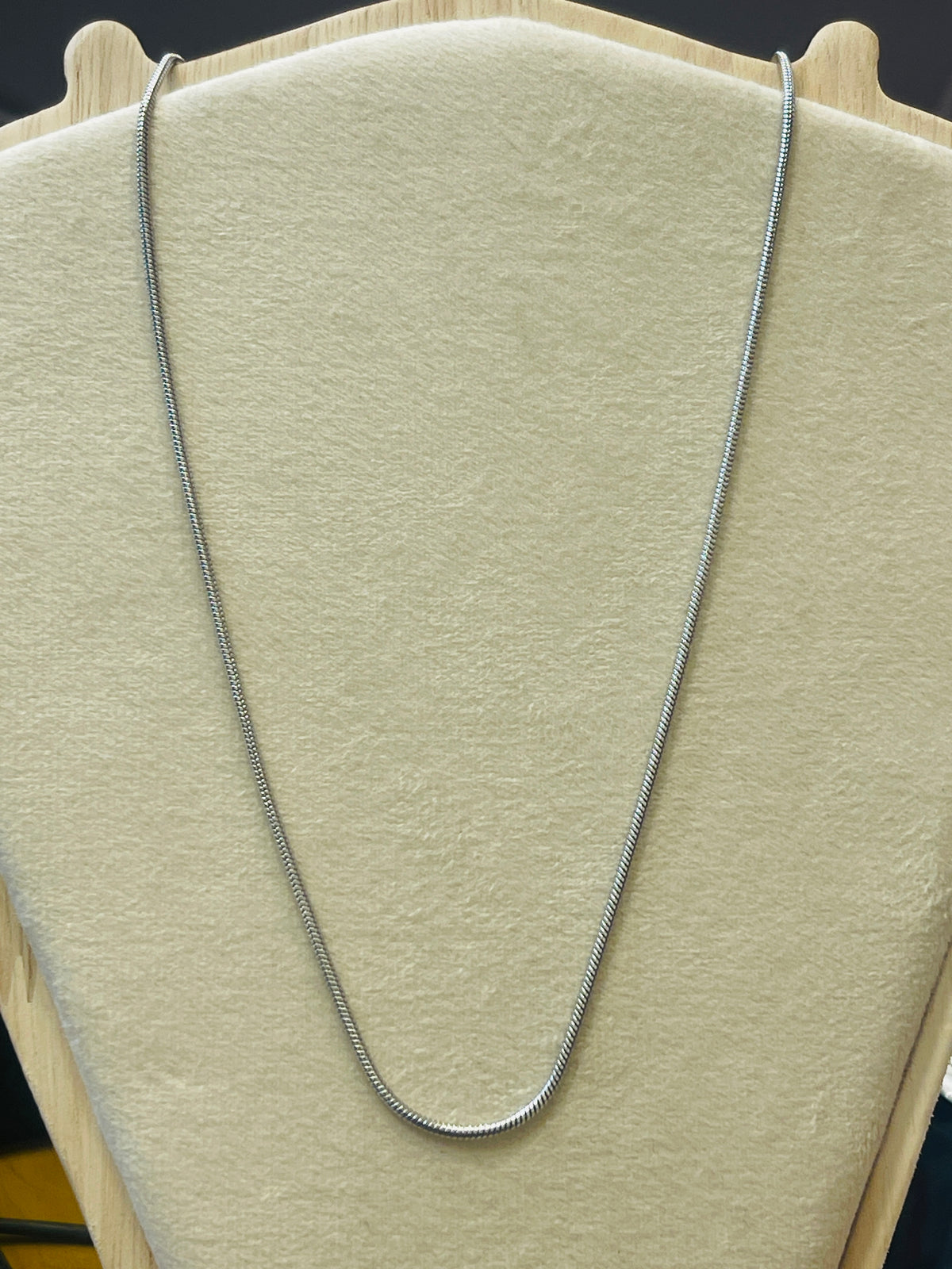 A silver snake chain necklace draped over a beige velvet jewelry display bust.