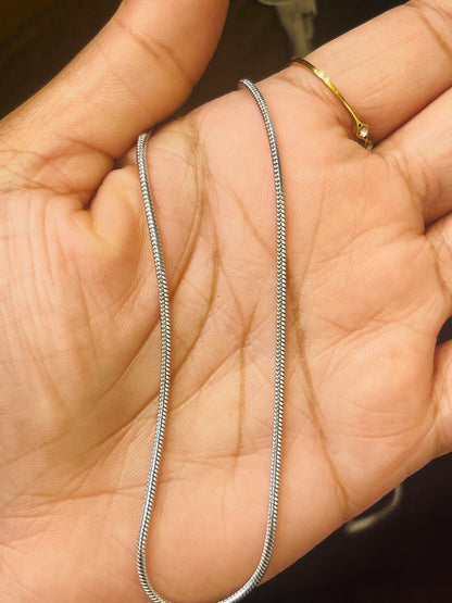 A silver snake chain necklace draped across an open hand, with a gold ring on the index finger.