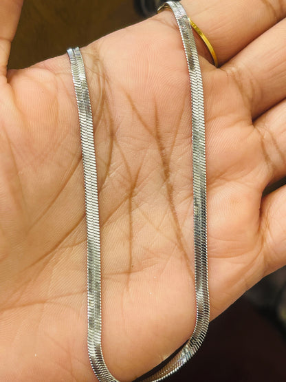 A close-up of a silver snake chain necklace draped across an open hand, with a gold ring visible on the finger for scale.