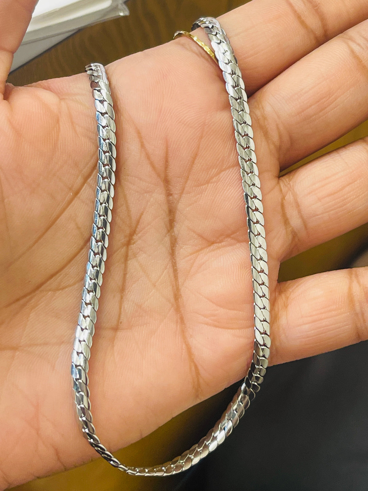 A silver-toned metal chain necklace with a textured, woven link design, draped over a person's hand.