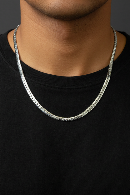 A close-up of a man's neck and chest wearing a silver chain necklace over a black t-shirt, against a dark gray background.