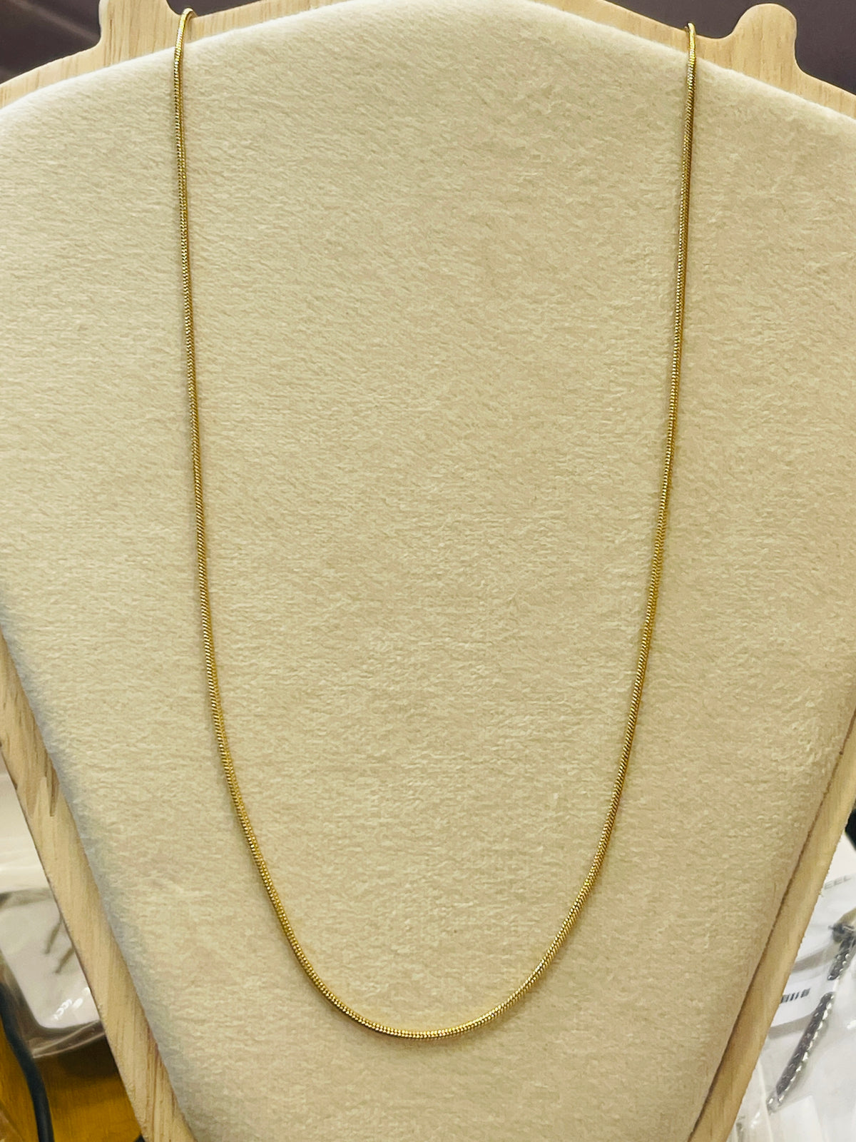 A delicate gold chain necklace draped over a beige fabric jewelry display bust.