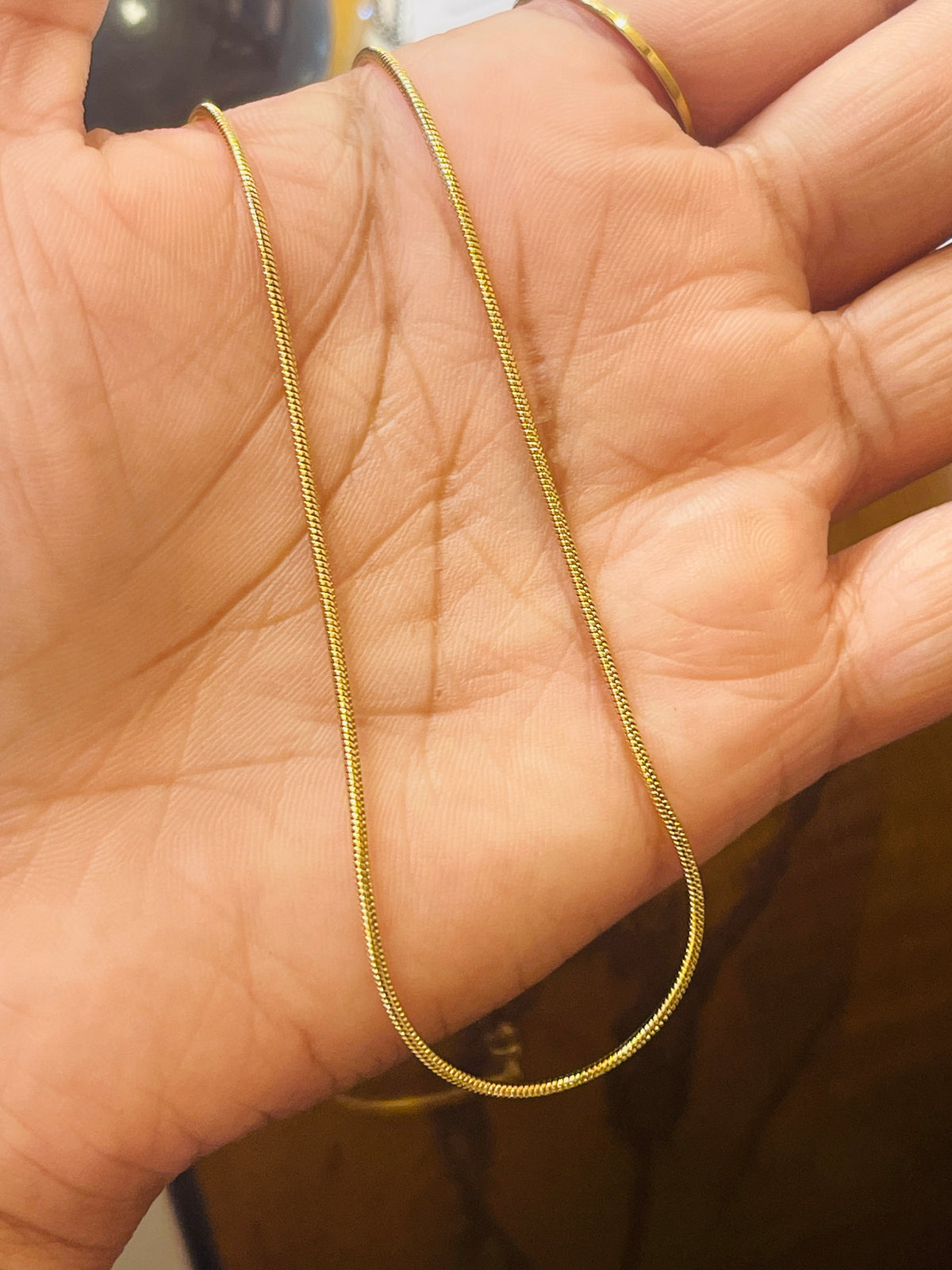 A delicate gold chain necklace draped over an open hand, showing its fine link structure against the skin.