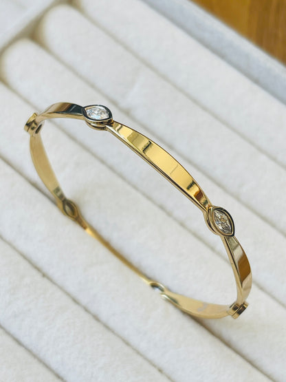 A polished yellow gold hinged bangle bracelet with two small marquise-cut clear gemstones, displayed on a white jewelry cushion.