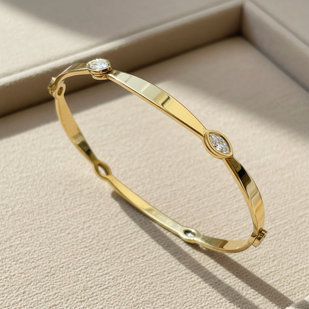 A polished gold bangle bracelet with two small oval-cut clear gemstones, displayed on a beige textured jewelry box.