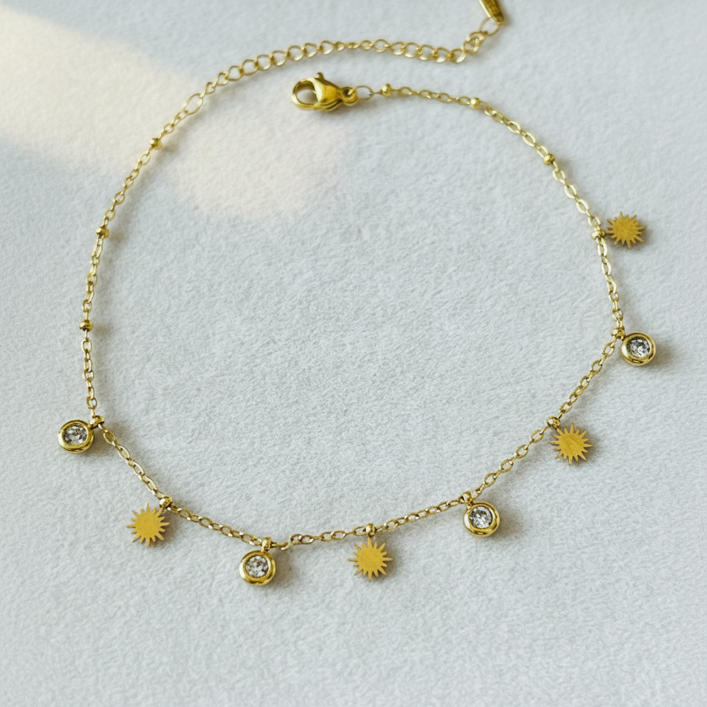 A delicate gold chain necklace with small sunburst charms and three clear crystal bezel settings, displayed on a textured light gray background.