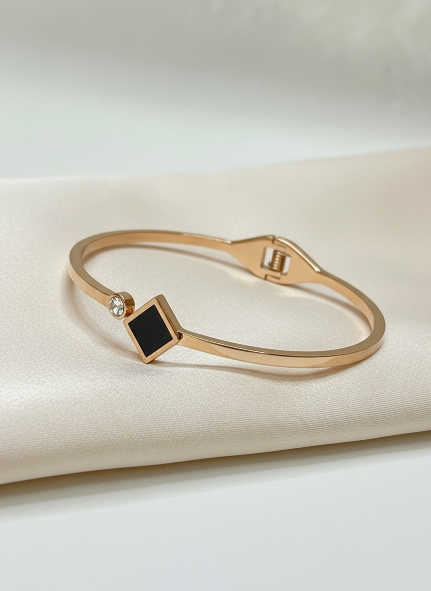 Rose gold bracelet with a black square stone on a beige fabric background