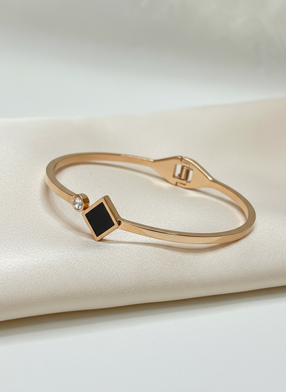 Rose gold bracelet with a black square stone on a beige fabric background