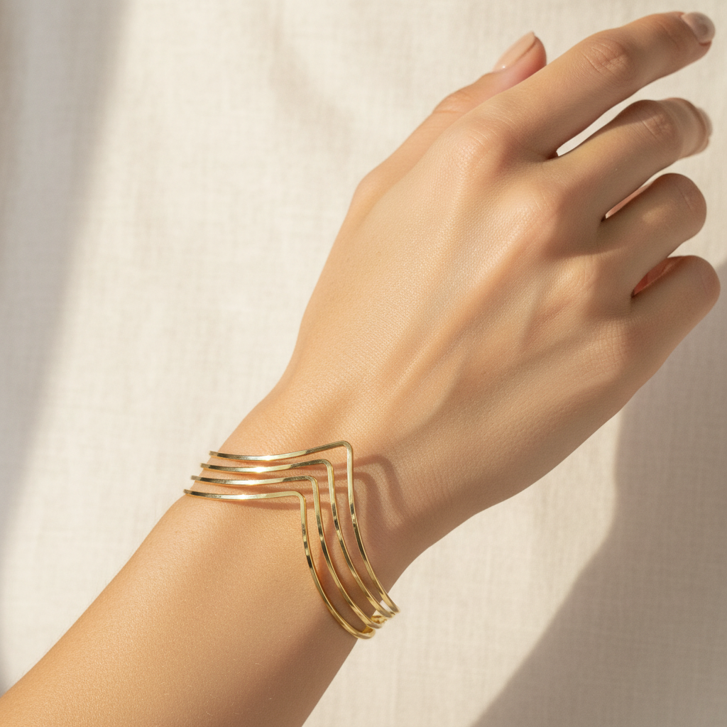 A gold-toned multi-band cuff bracelet worn on a woman's wrist, shown against a warm, sunlit neutral fabric background.