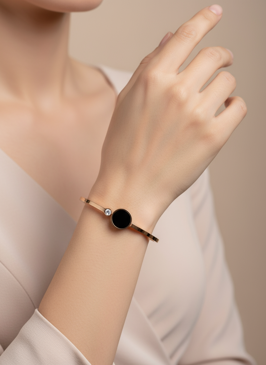Close-up of a wrist wearing a delicate bracelet with a black gemstone on a neutral background
