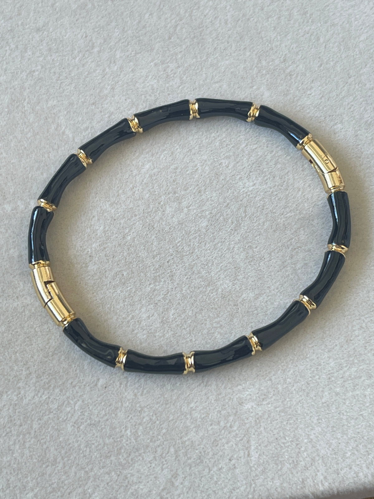 A beaded stretch bracelet featuring glossy black cylindrical beads separated by gold-toned metal spacer rings, displayed on a textured light gray surface.