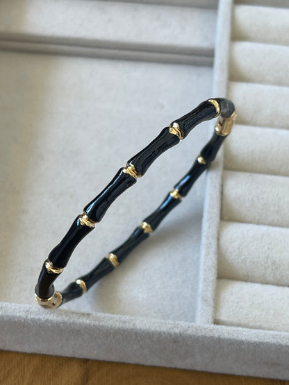 A black and gold bamboo-style bangle bracelet displayed inside a light gray jewelry box.
