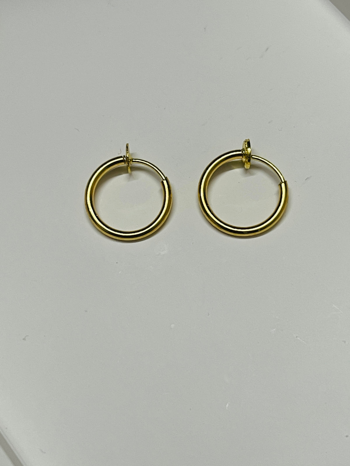A pair of gold hoop earrings with a polished finish, displayed on a plain light gray surface.