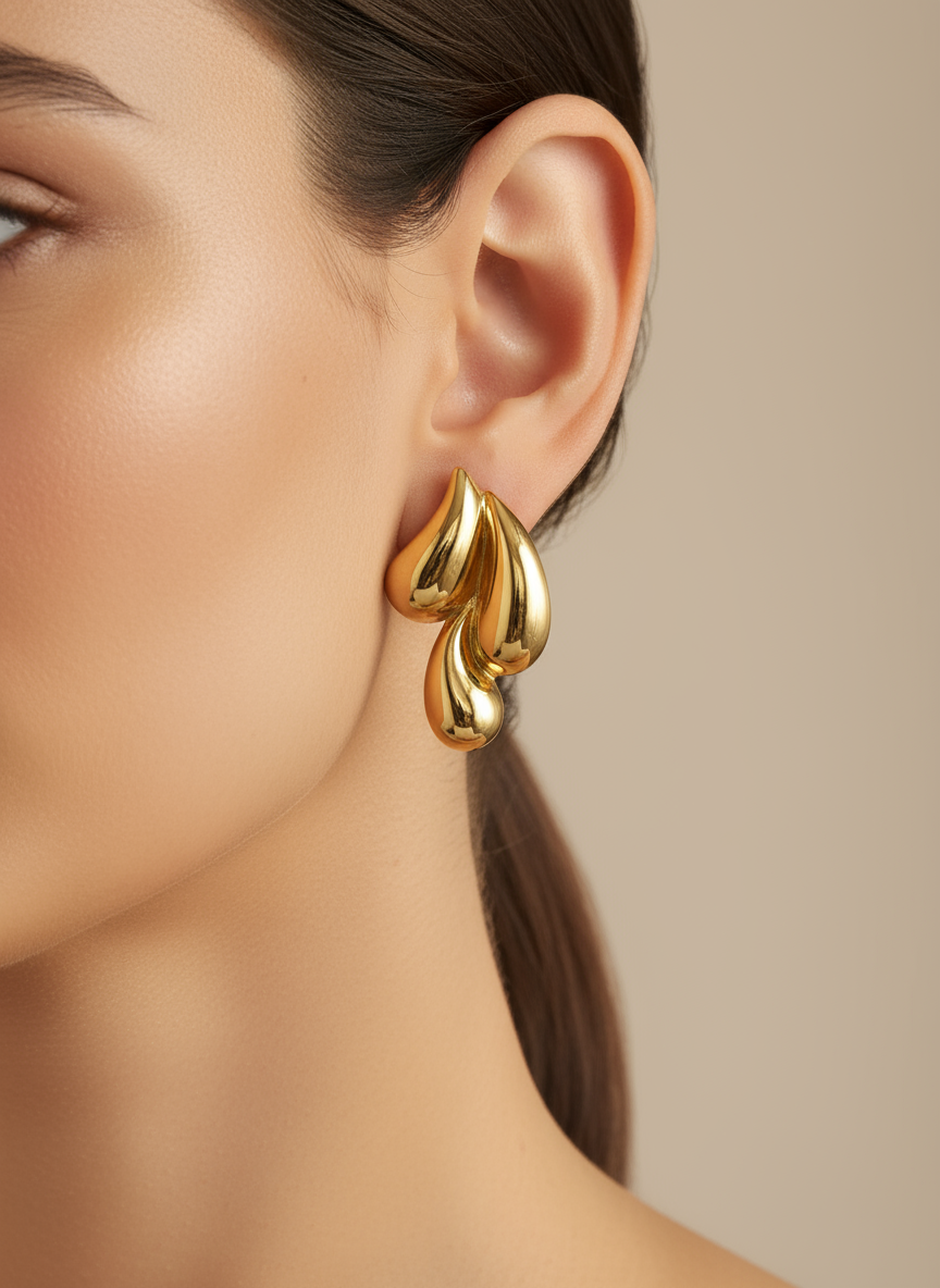 Gold leaf-shaped earrings on a white surface with a white flower in the background