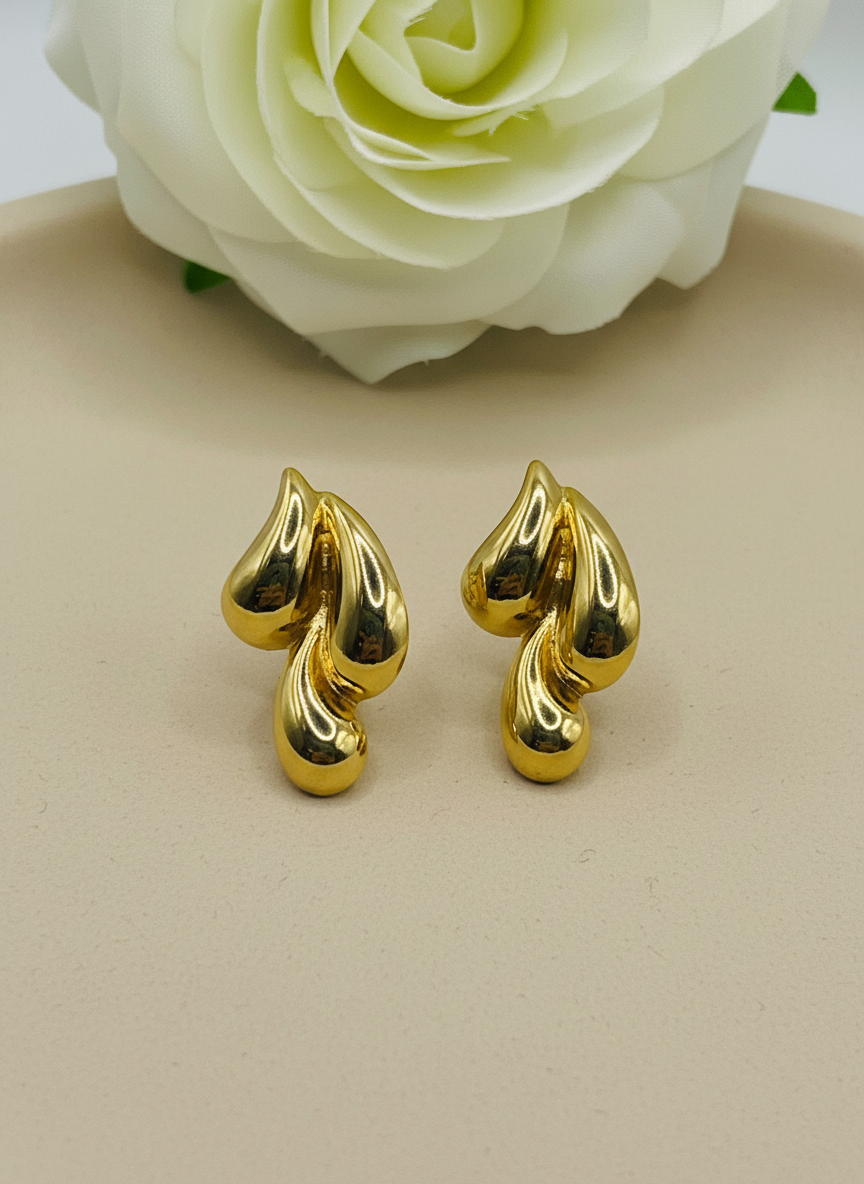 Gold leaf-shaped earrings on a white surface with a white flower in the background