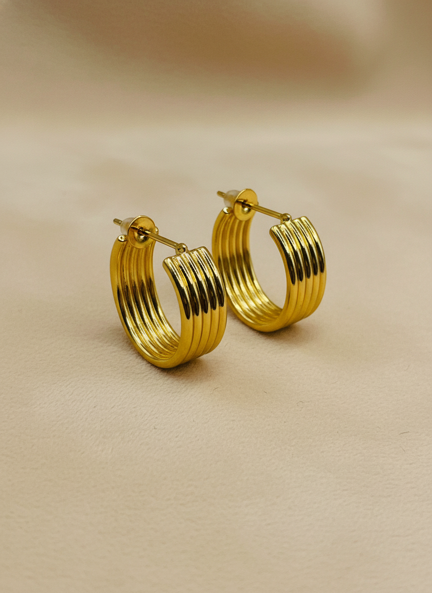 Gold hoop earrings on a white surface with a white flower in the background