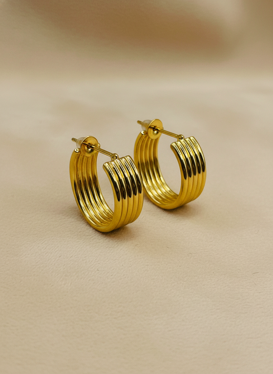 Gold hoop earrings on a white surface with a white flower in the background