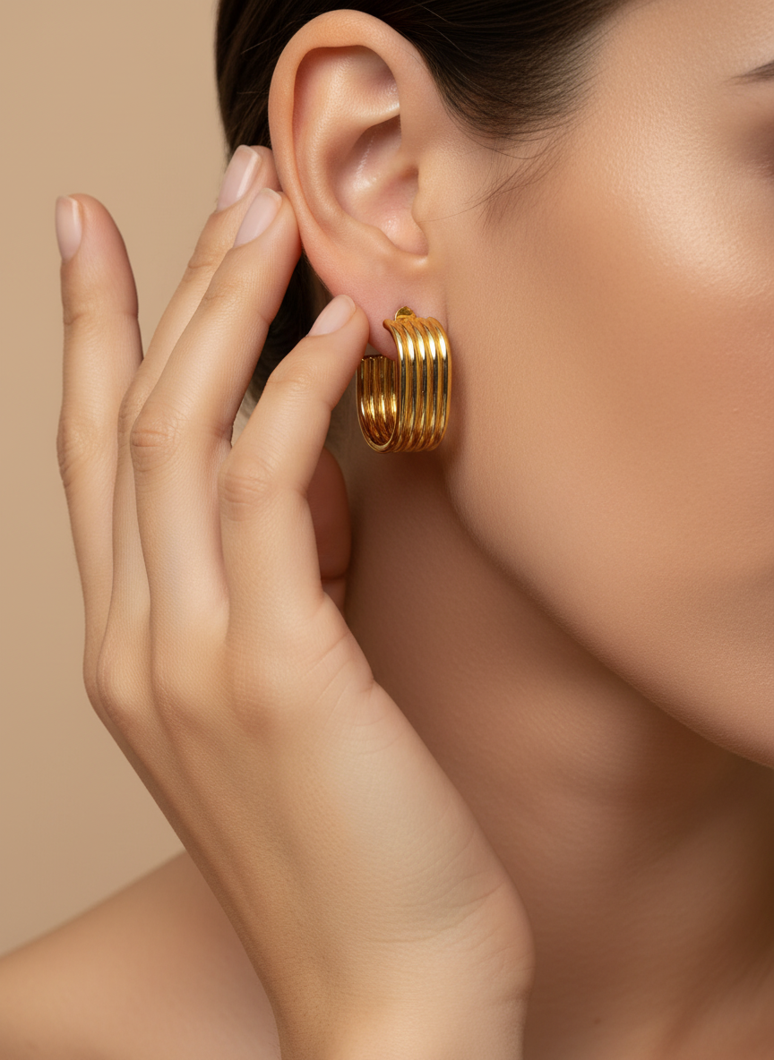 Gold hoop earrings on a white surface with a white flower in the background