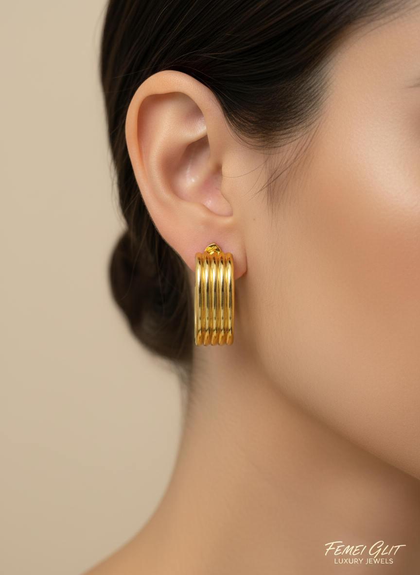 Gold hoop earrings on a white surface with a white flower in the background