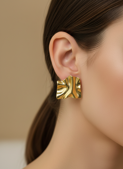 Gold leaf-shaped earrings on a white beaded background