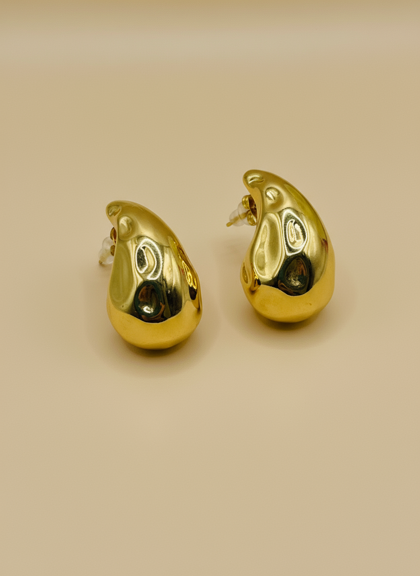 Gold teardrop-shaped earrings on a white surface with a floral background