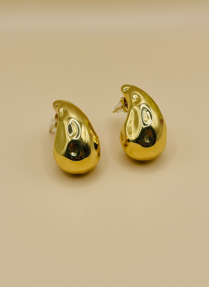 Gold teardrop-shaped earrings on a white surface with a floral background