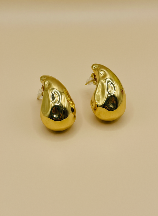 Gold teardrop-shaped earrings on a white surface with a floral background