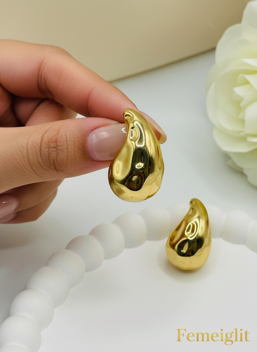 Gold teardrop-shaped earrings on a white surface with a floral background
