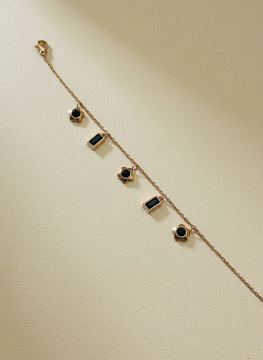Rose Gold chain bracelet with black gemstones on a light gray background