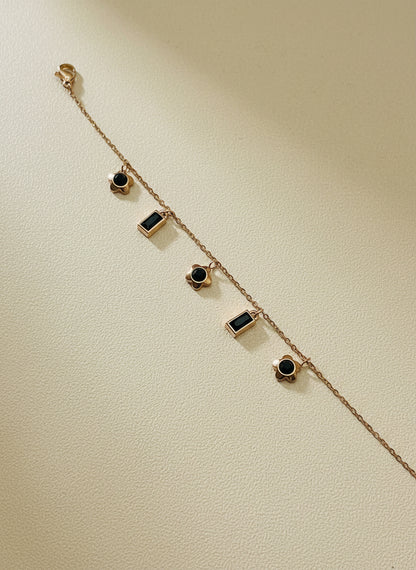 Rose Gold chain bracelet with black gemstones on a light gray background