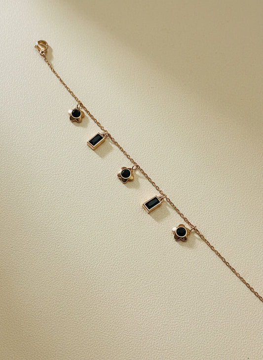 Rose Gold chain bracelet with black gemstones on a light gray background