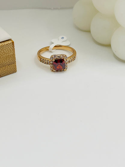 Gold ring with a red gemstone on a white surface
