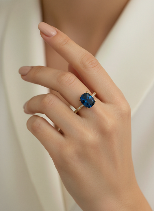 Hand wearing a ring with a blue gemstone against a neutral background
