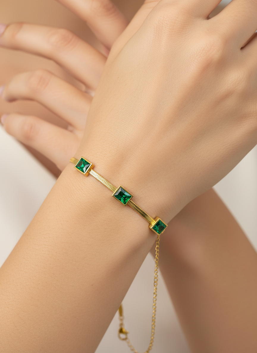 Gold bracelet with green gemstones on a wrist against a neutral background