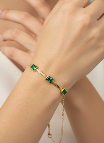 Gold bracelet with green gemstones on a wrist against a neutral background