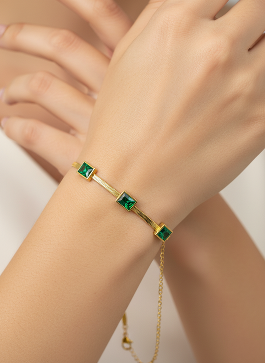 Gold bracelet with green gemstones on a wrist against a neutral background